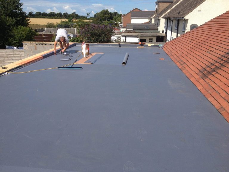 Roofer installing a new flat roof membrane beside a tiled roof