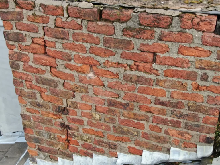 Brickwork: Crumbling and receded mortar joints between red bricks on an older house wall